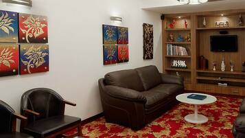 A living room with a brown leather sofa, a red patterned carpet, and a bookshelf with various items.