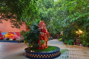 A courtyard with a statue, lush greenery, and a mural on the wall.