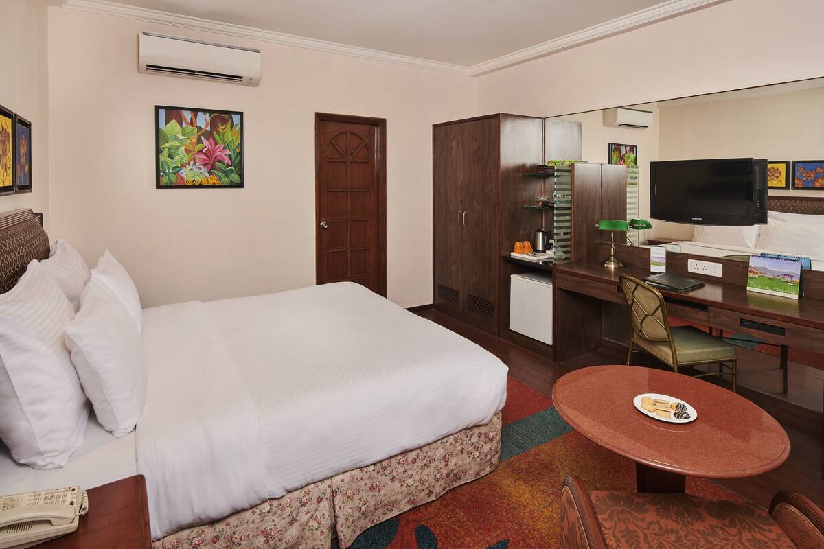 Habitación de hotel con cama, escritorio, silla, televisor y una pequeña kitchenette.