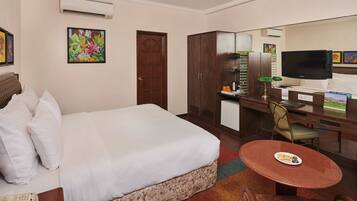 A hotel room with a bed, a desk, a chair, a television, and a small kitchenette.