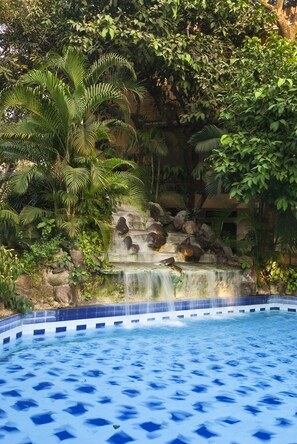 A pool with a waterfall feature surrounded by lush greenery.