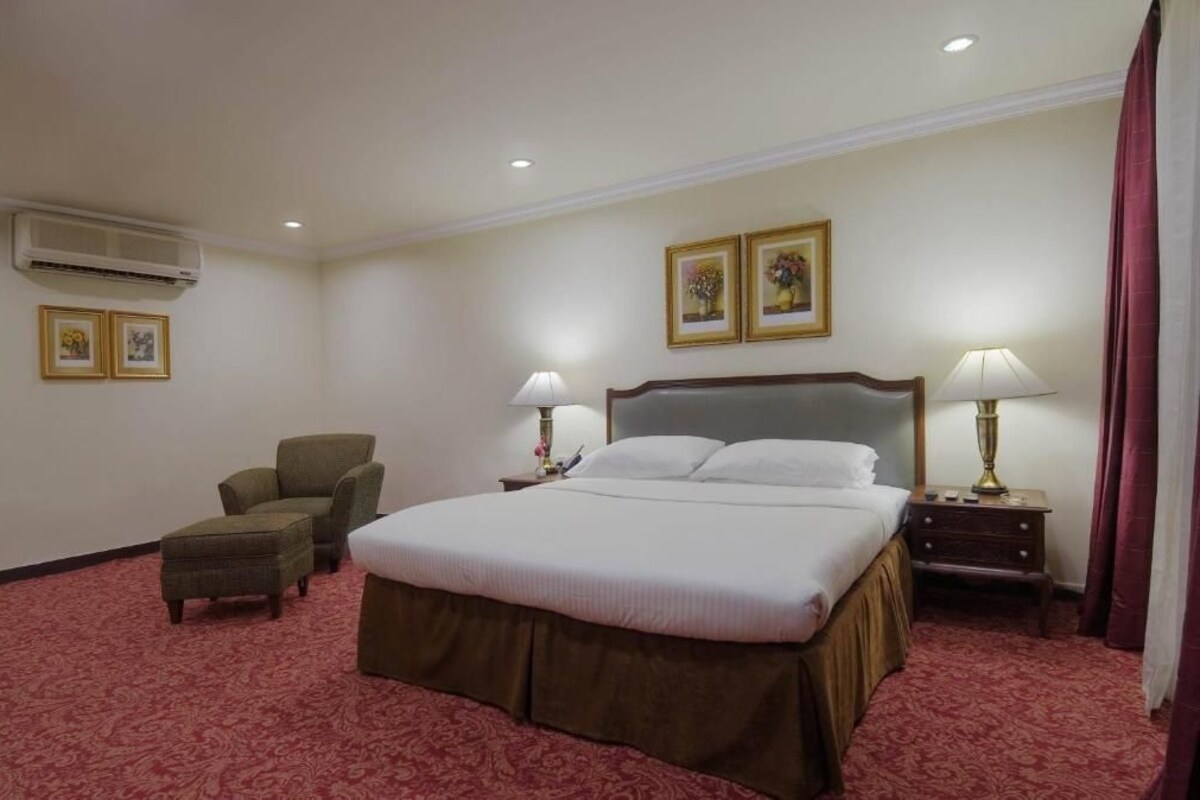 Une chambre d’hôtel avec un grand lit, deux tables de chevet avec des lampes, une chaise et un appareil de climatisation.