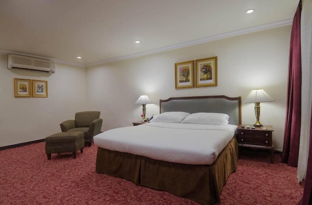 Habitación de hotel con una cama grande, dos mesitas de noche con lámparas, una silla y un aire acondicionado.