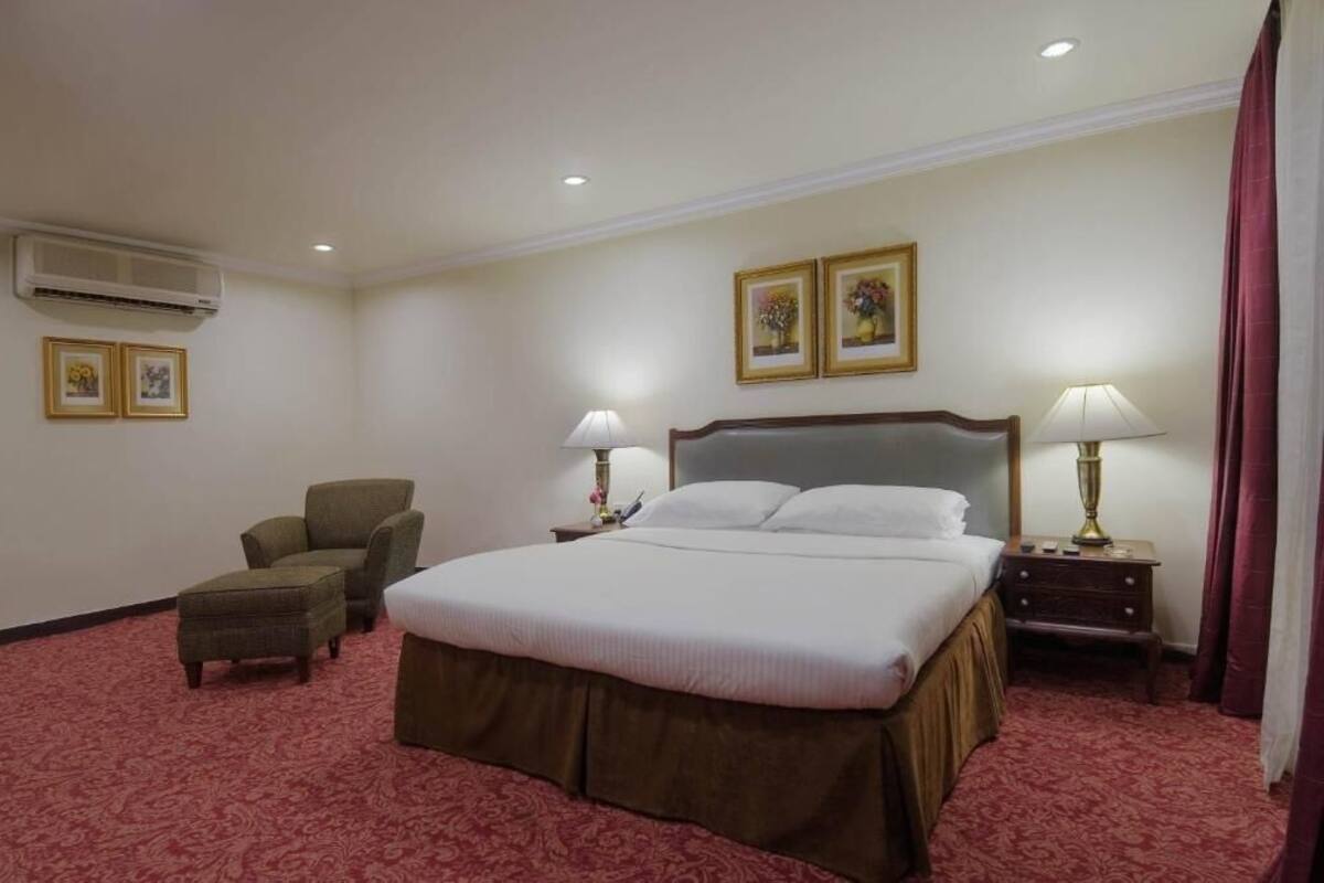 Habitación de hotel con una cama grande, dos mesitas de noche con lámparas, una silla y un aire acondicionado.