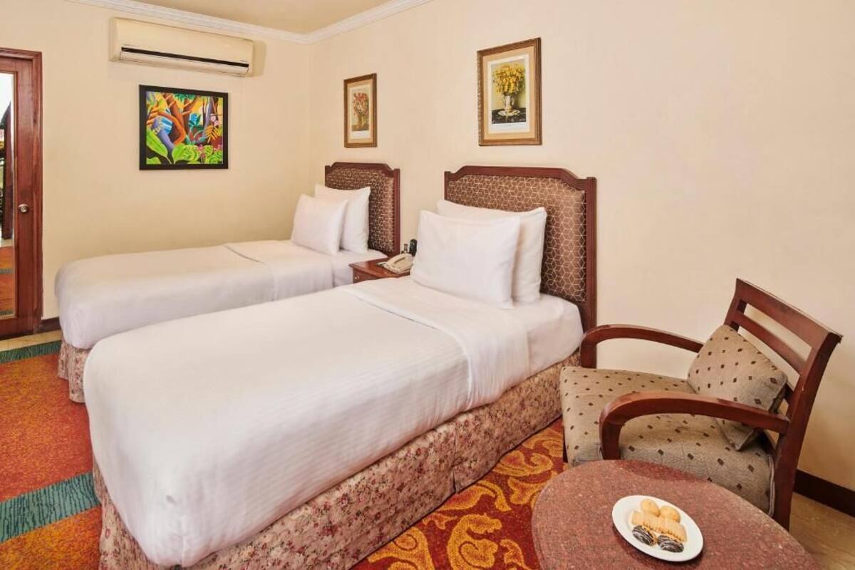 Habitación de hotel con dos camas, una silla, una mesita con un plato de comida y un cuadro en la pared.