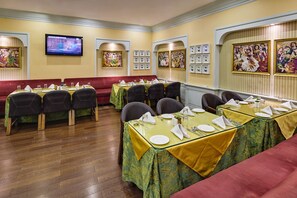 A restaurant with multiple tables set for dining, a television mounted on the wall, and various framed artworks on the walls.