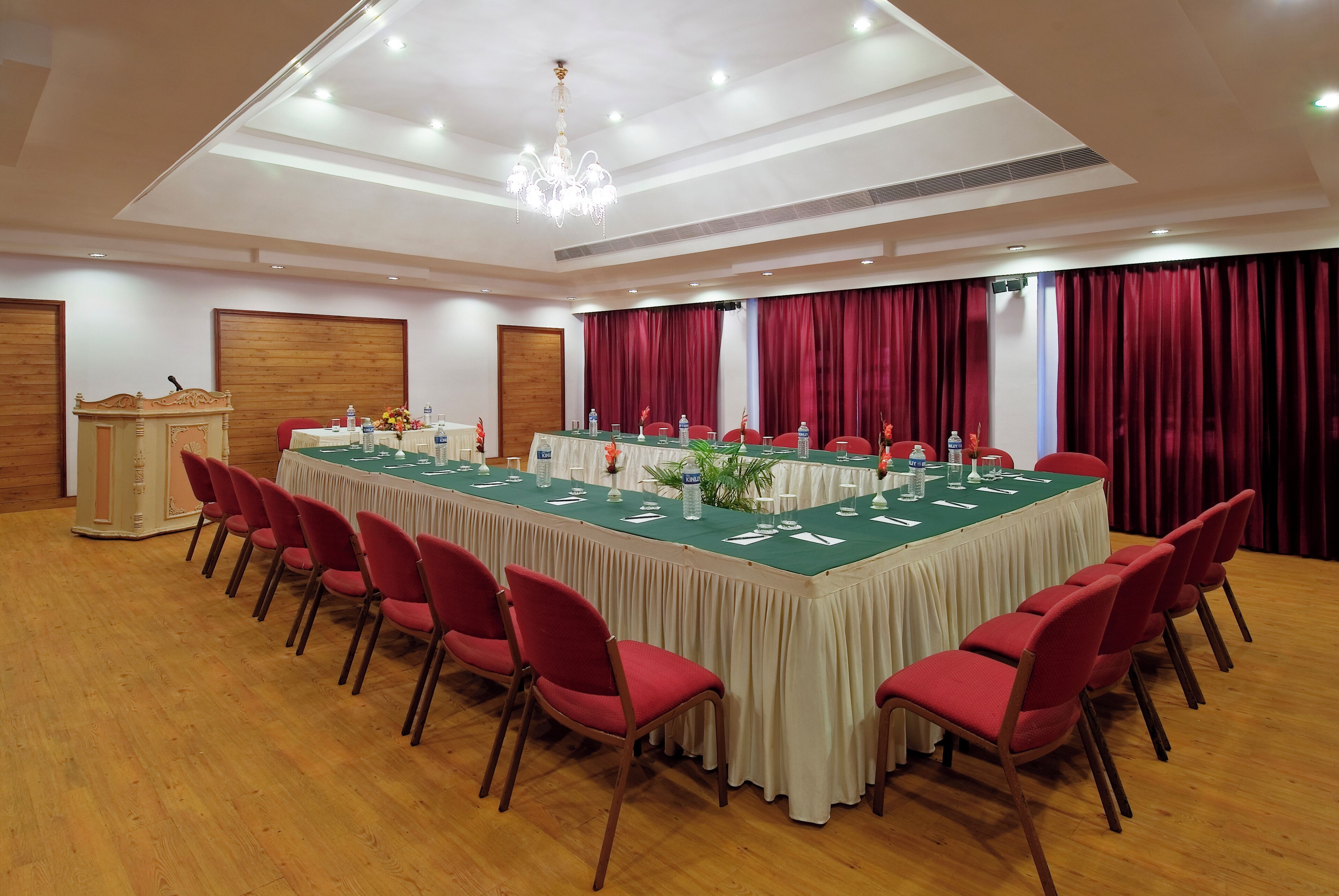 Uma sala de conferências com uma mesa comprida, cadeiras vermelhas e um pódio.