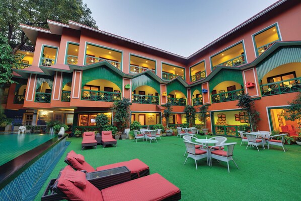 A hotel with multiple balconies, a swimming pool, and outdoor seating areas.