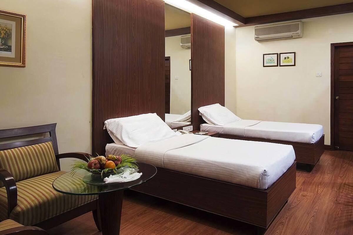 Una habitación de hotel con dos camas, una mesita con fruta, una silla y un espejo.