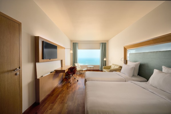 Habitación de hotel con una cama grande, un escritorio, una silla, un televisor y vista al océano.