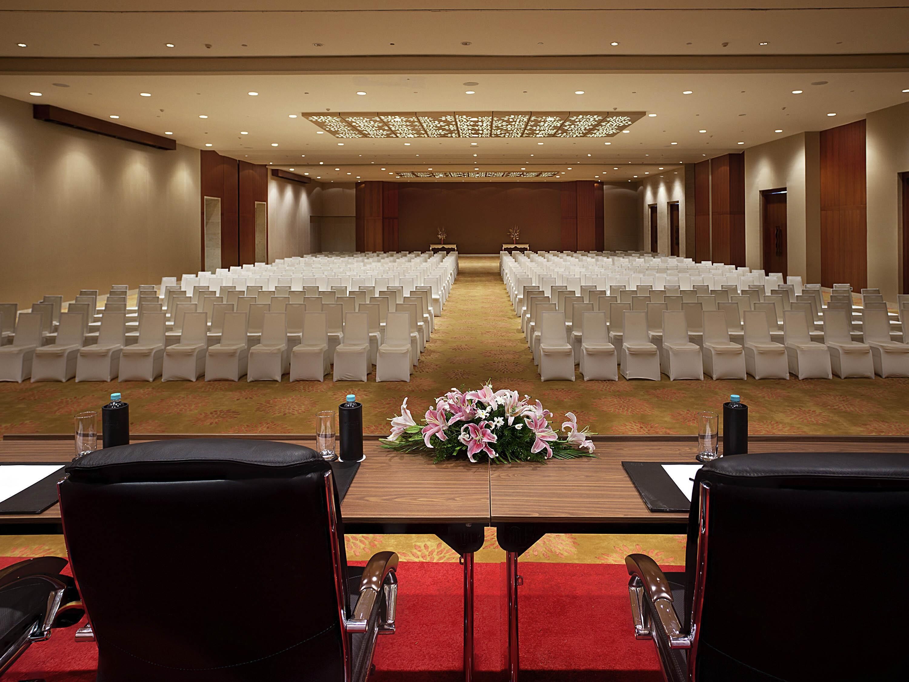 A conference room with rows of white chairs, a red carpet, and a floral centerpiece on the table.
