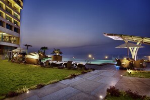 A well-lit outdoor lounge area with seating and a view of the ocean at dusk.