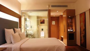 Habitación de hotel con una cama grande, cabina de ducha de vidrio, un mueble pequeño y un cuadro en la pared.