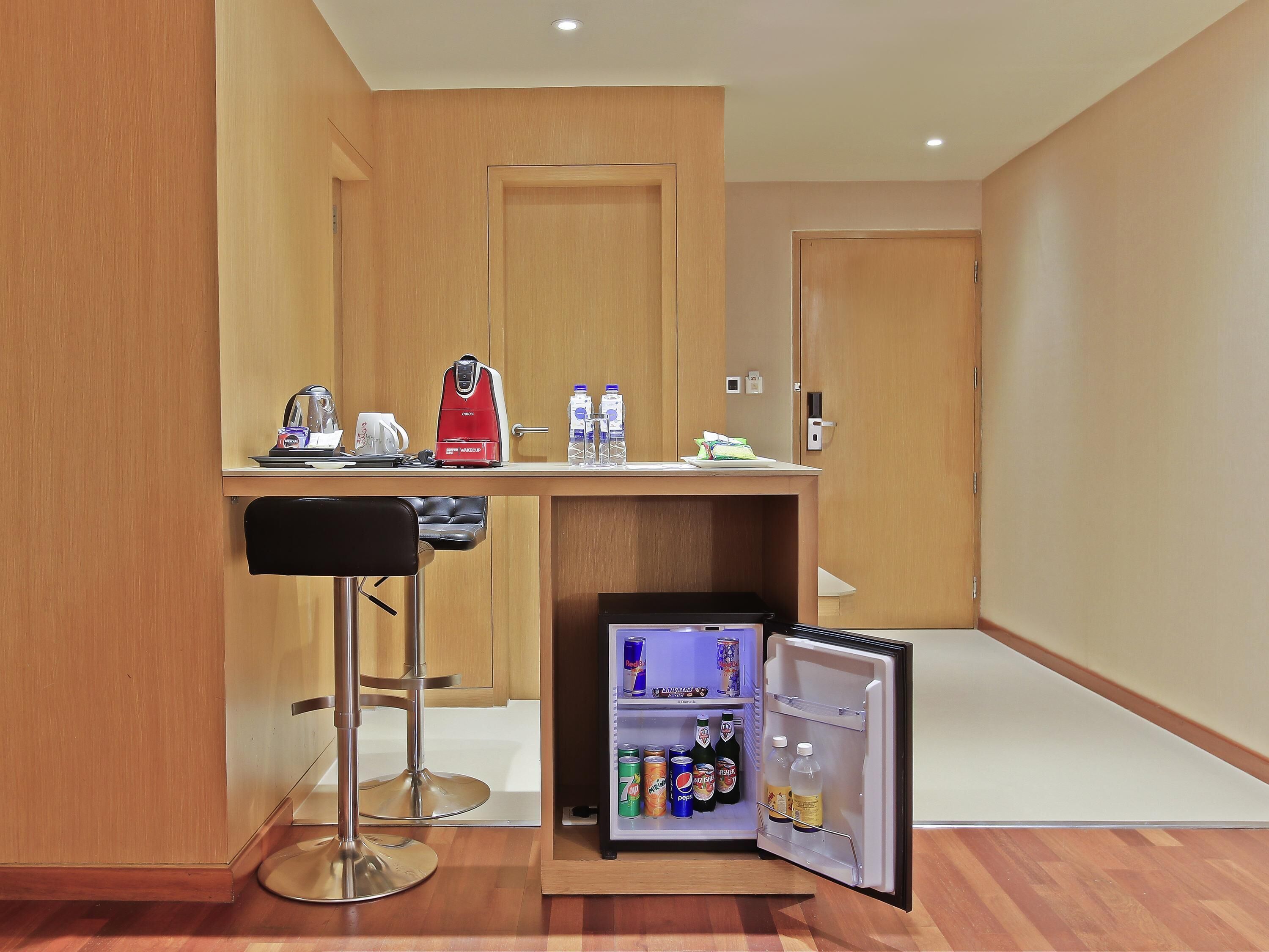 A compact kitchenette with a coffee maker, a mini-fridge stocked with beverages, and a bar stool.