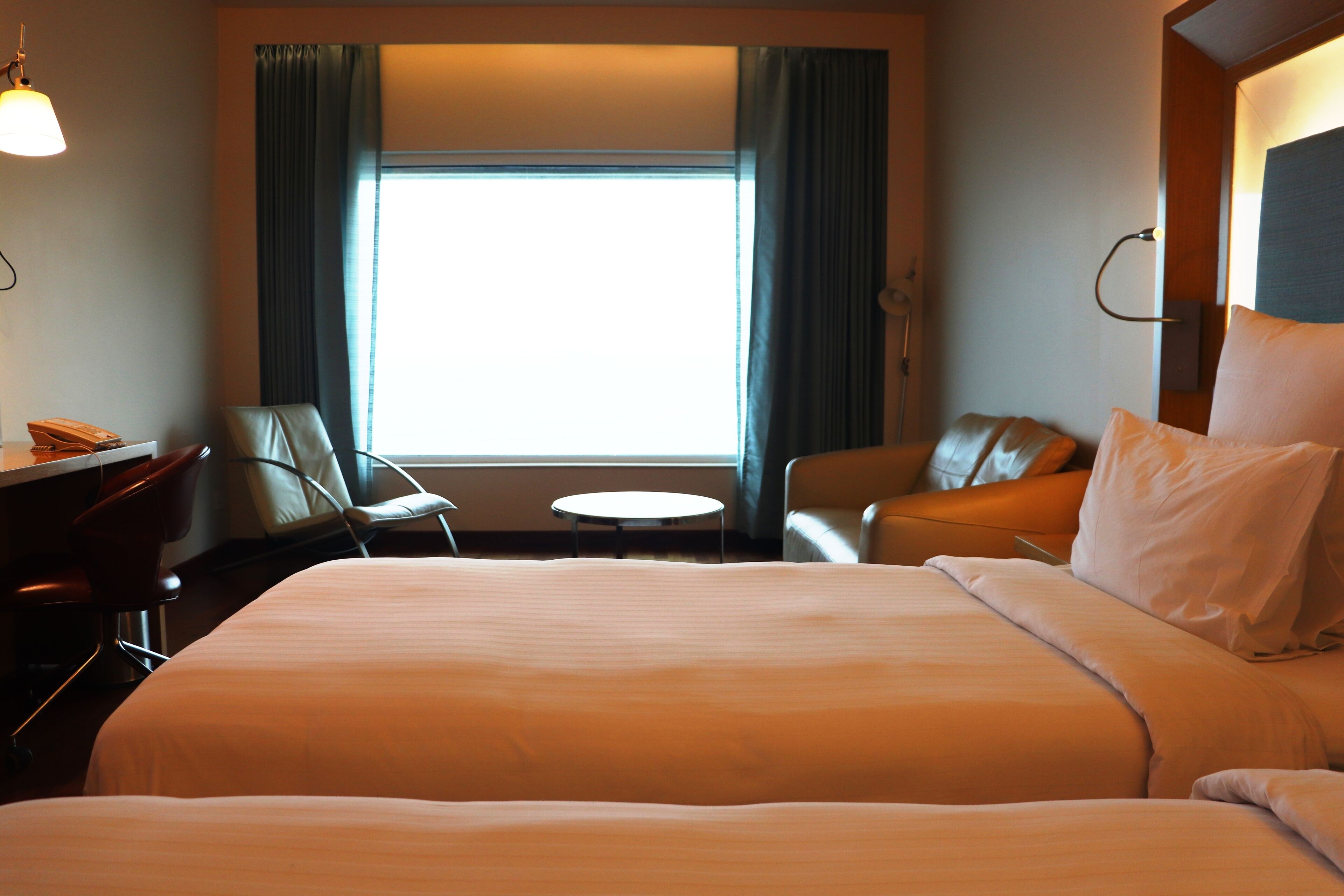 A hotel room with a large bed, two chairs, a desk, and a window with curtains.