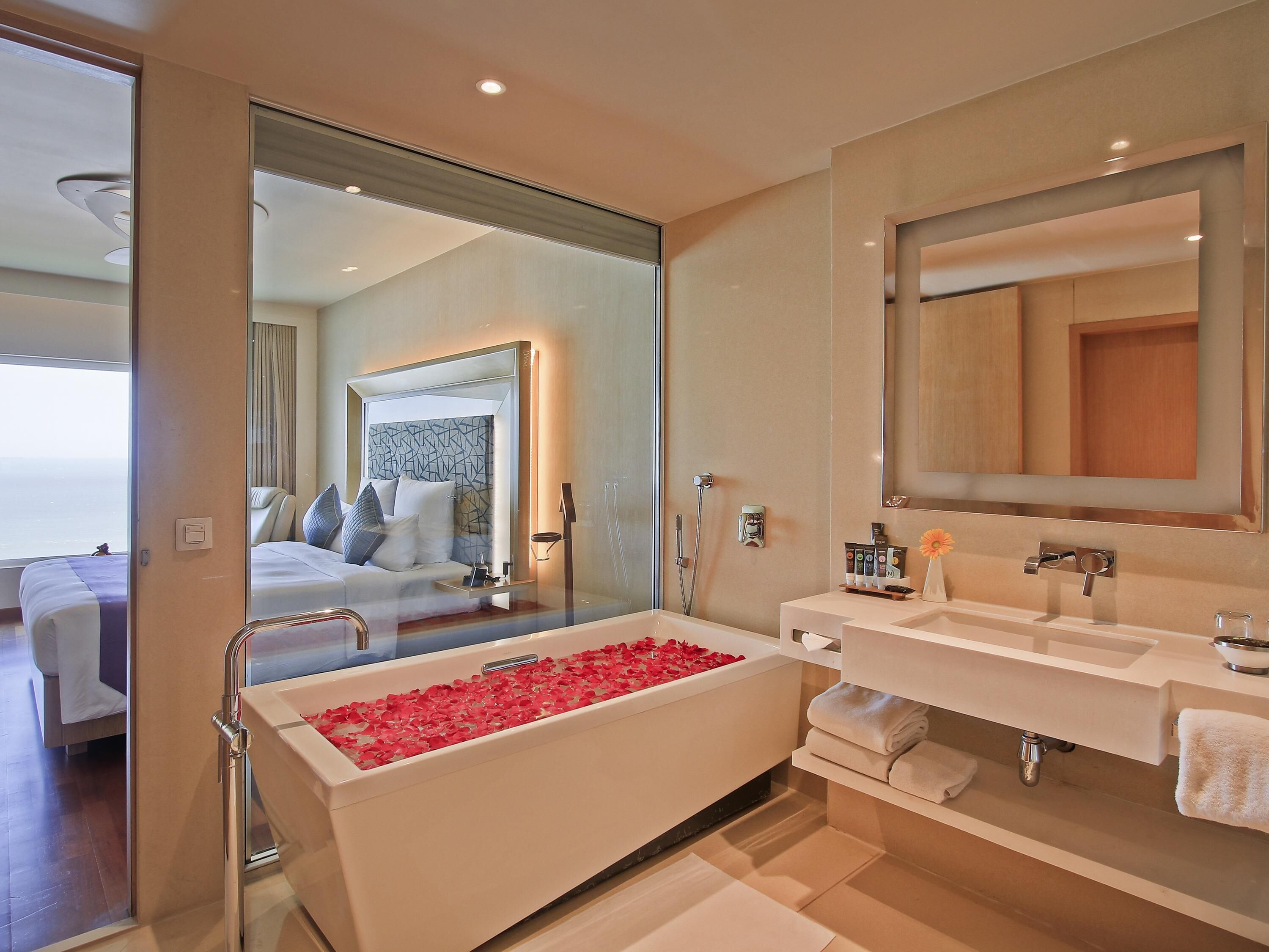 Un baño moderno de hotel con una bañera llena de pétalos de rosa, un espejo grande y una ducha.