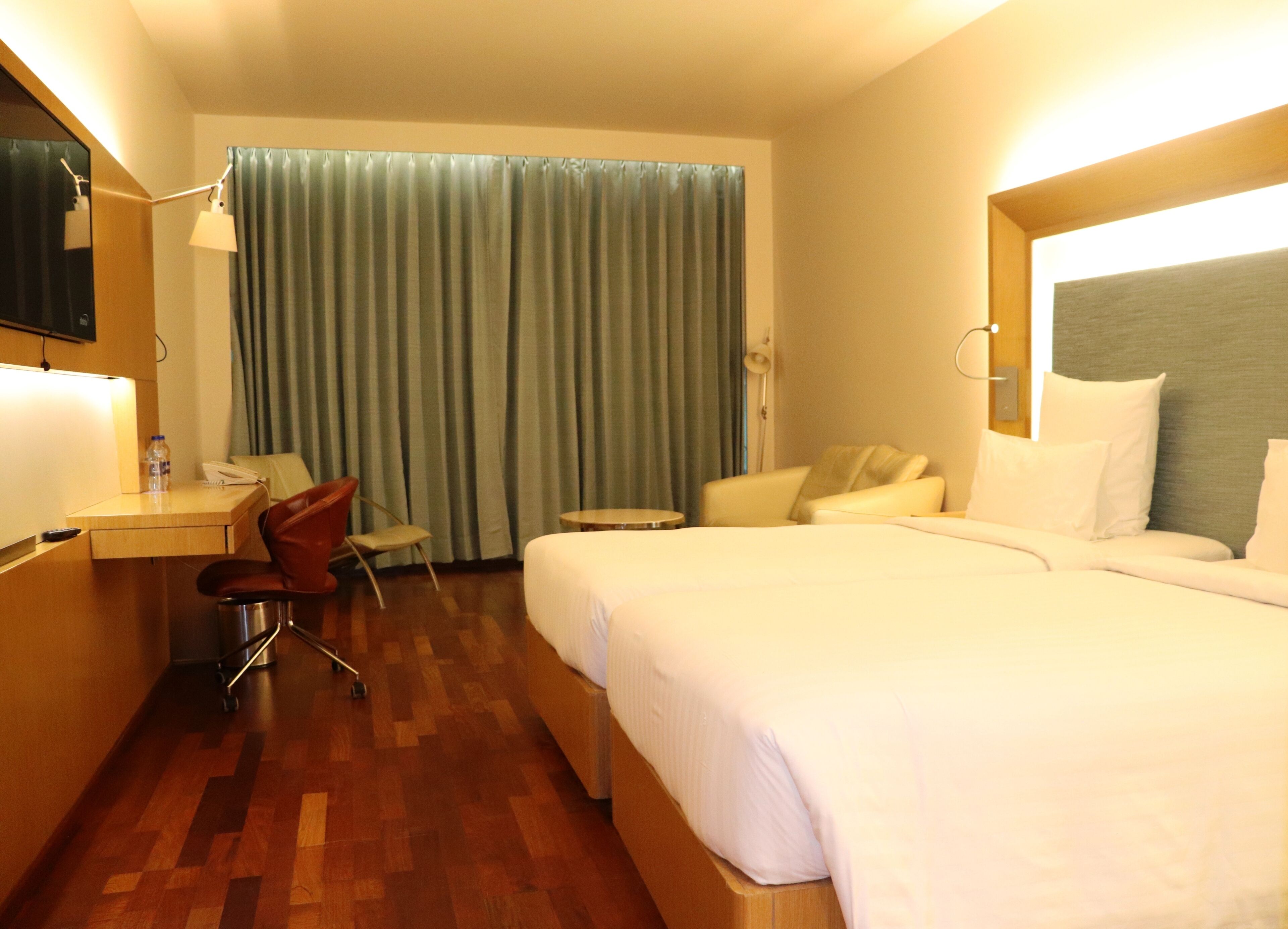 A hotel room with a bed, a desk with a chair, a small table, and a curtain.