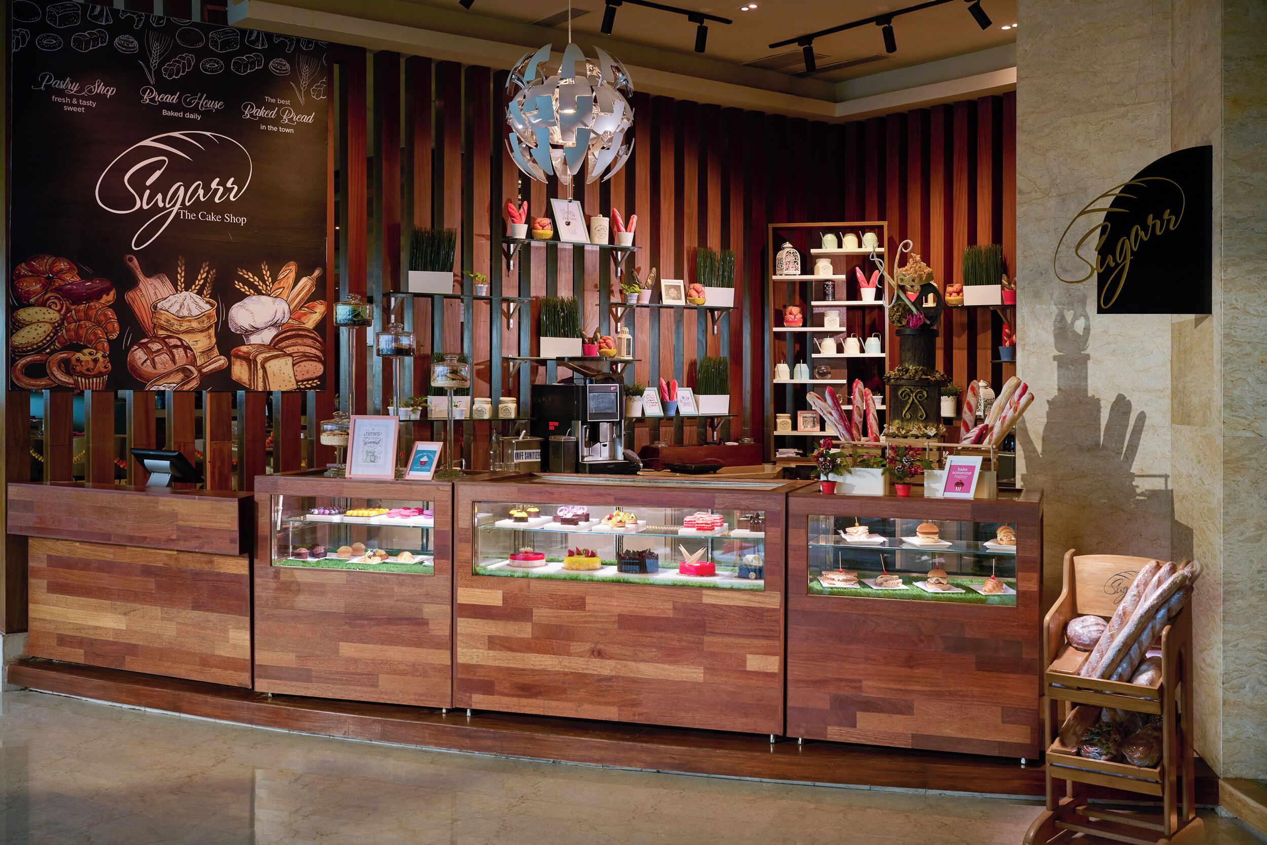 A bakery display with various baked goods and a sign reading "Sugarr The Cake Shop".