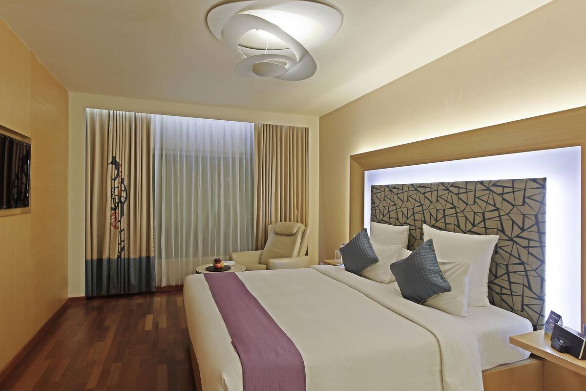 Ein Hotelzimmer mit einem großen Bett, einem Sessel, einem Nachttisch und einer modernen Deckenleuchte.