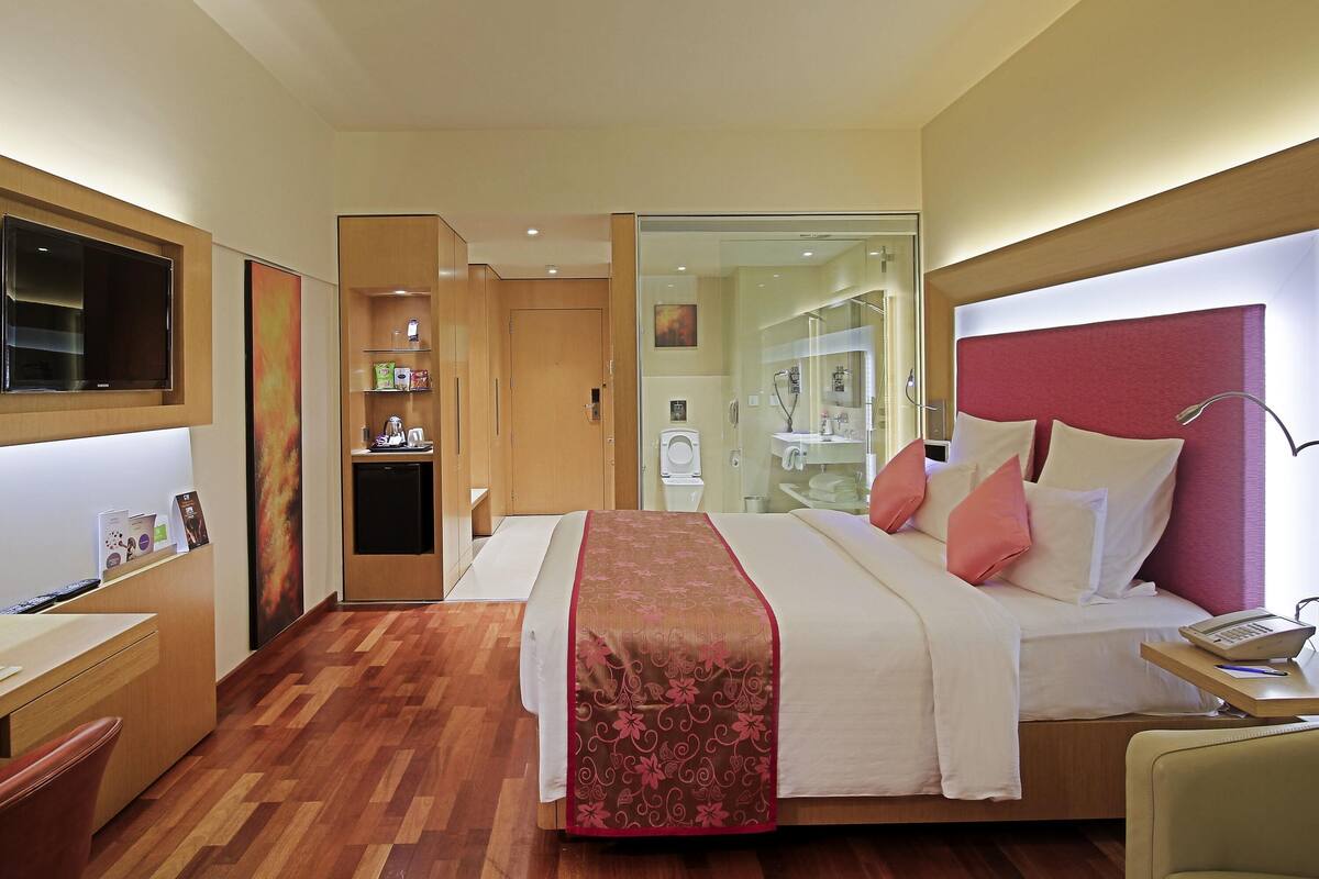 Une chambre d’hôtel comprenant un lit, une table de chevet, un bureau, une armoire et une salle de bain visible à travers une porte en verre.