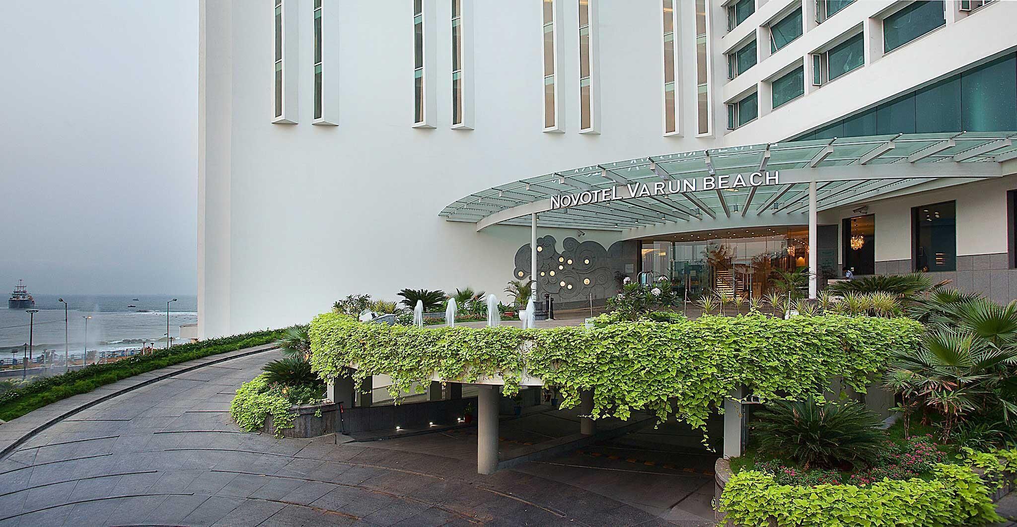 A modern hotel with a glass facade, a covered entrance, and a landscaped garden area.