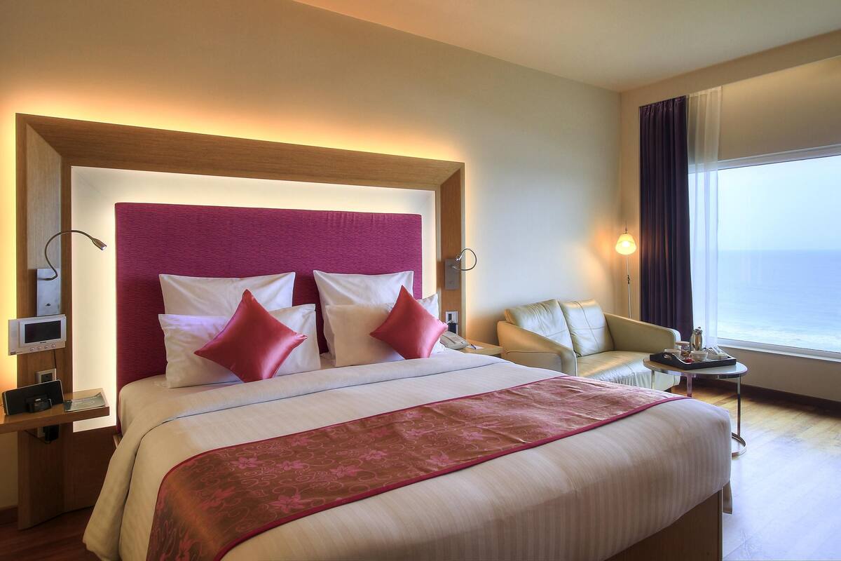Une chambre d’hôtel avec un grand lit, une table de chevet avec une lampe, une chaise et une vue sur la mer.