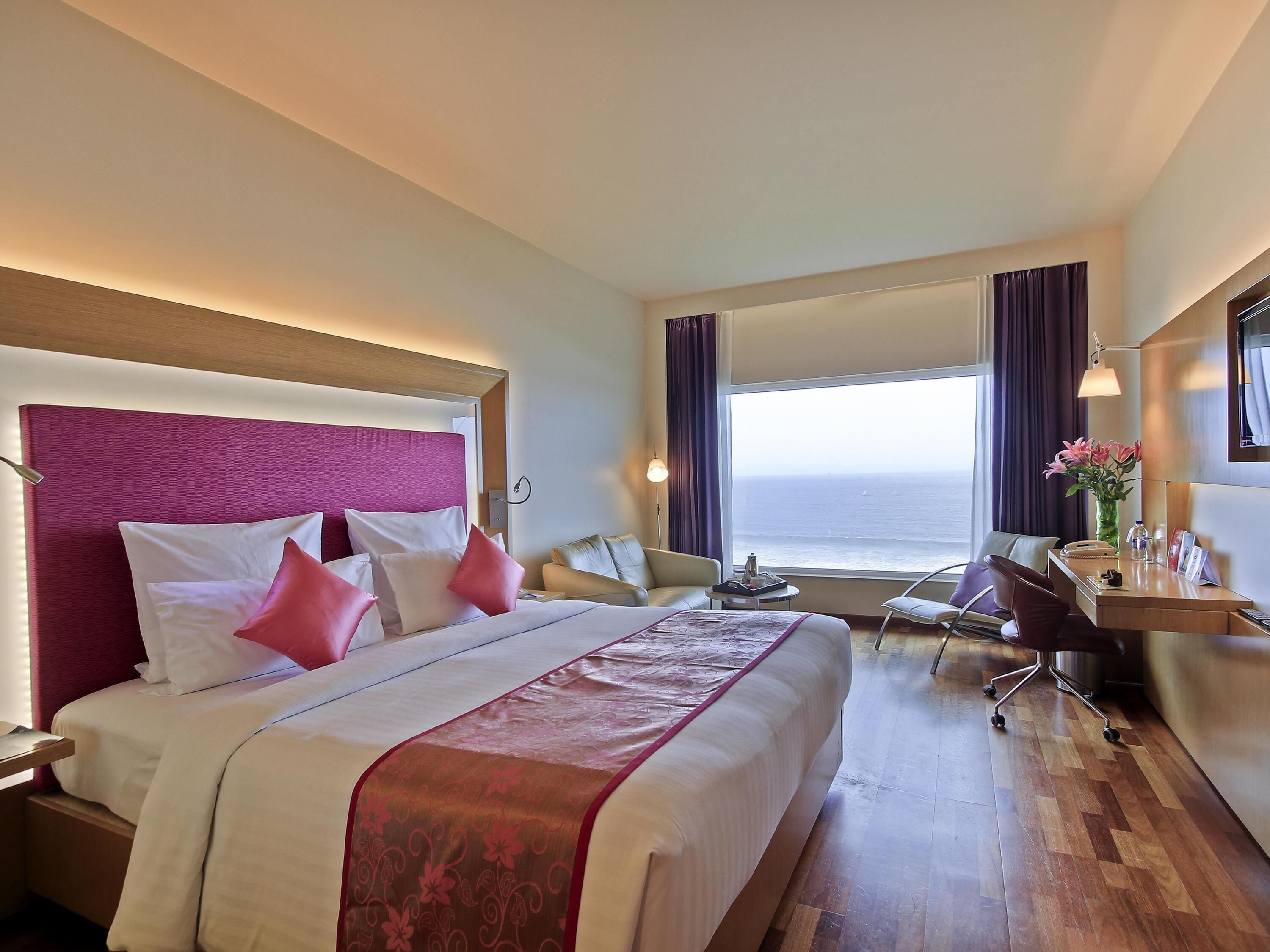 A hotel room with a large bed, a desk, a chair, and a view of the sea.