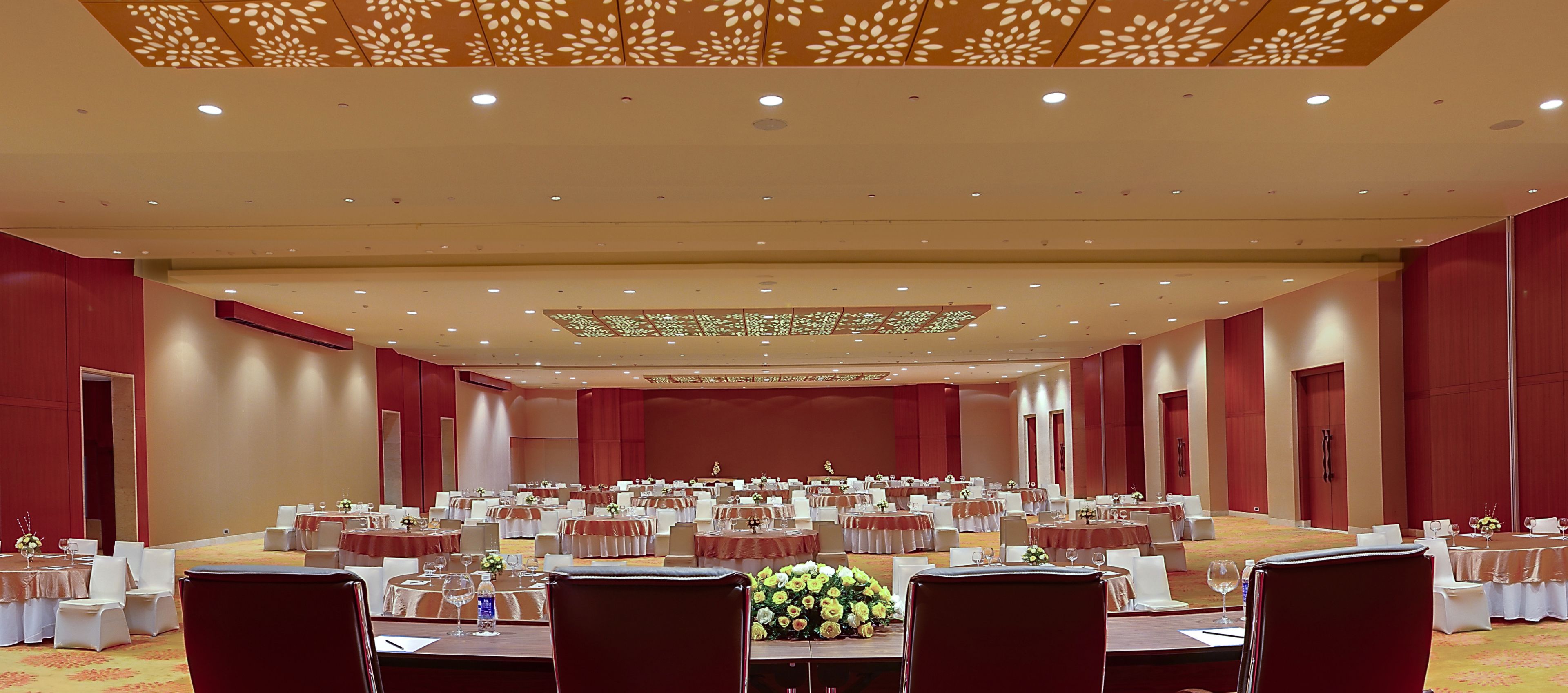 Une grande salle de banquet avec de nombreuses tables rondes, des chaises blanches et des rideaux rouges.