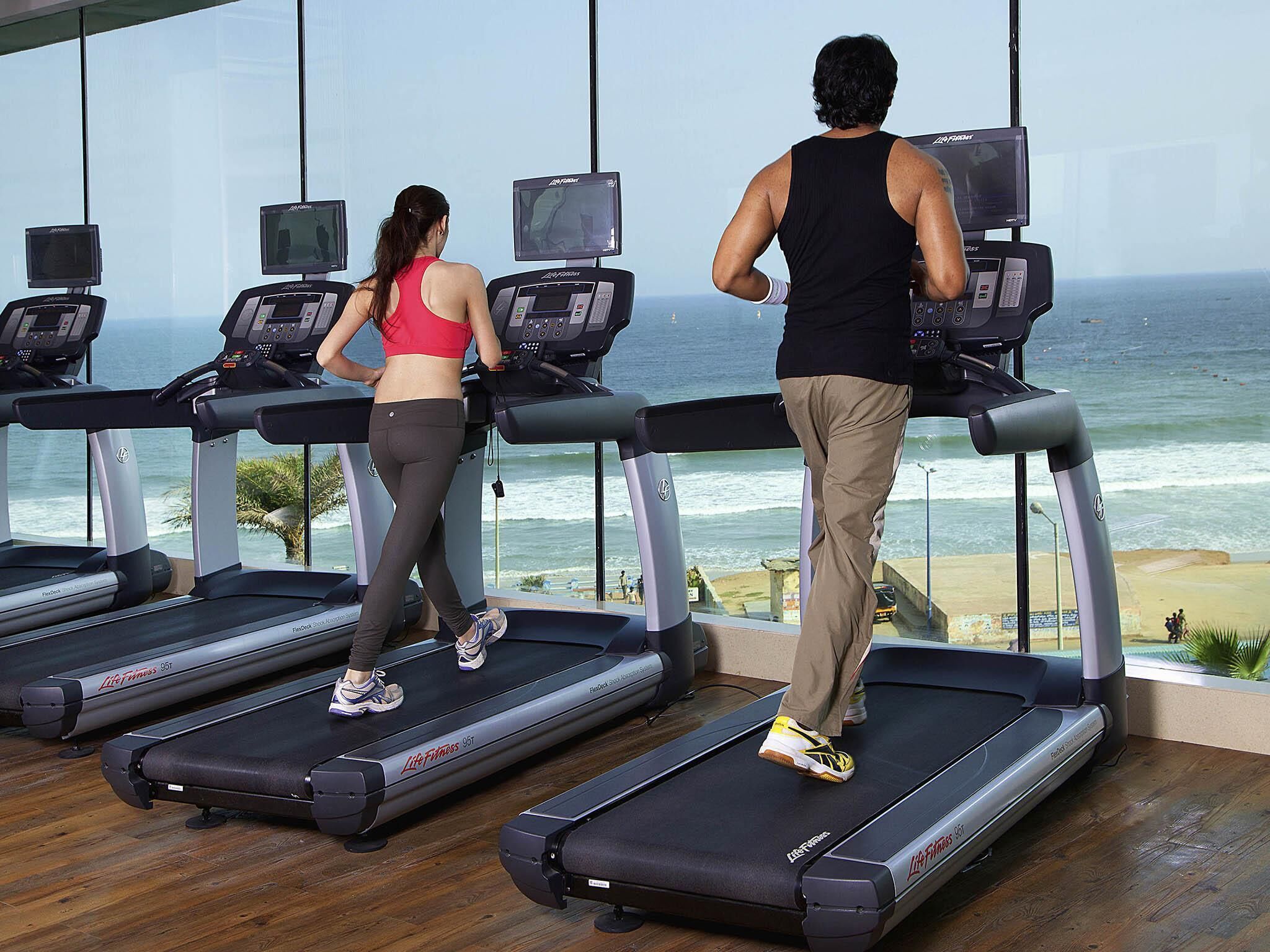 A gym with treadmills, large windows, and a view of the ocean.