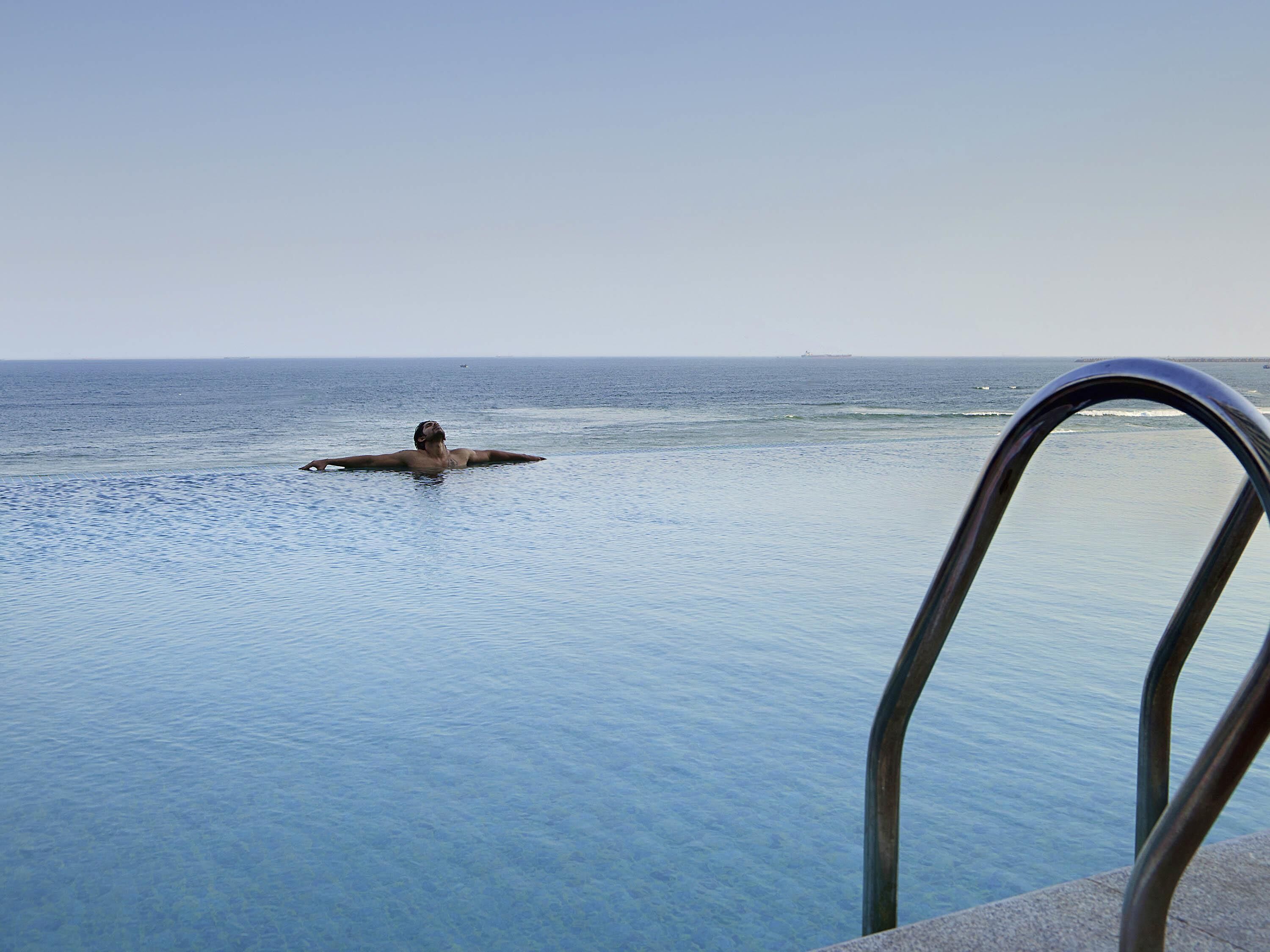 Uma pessoa em uma piscina com vista para o oceano e um navio ao longe.