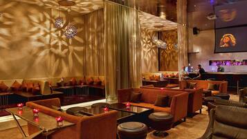 A modern lounge area with sofas and tables, a bar in the background, and decorative lighting.