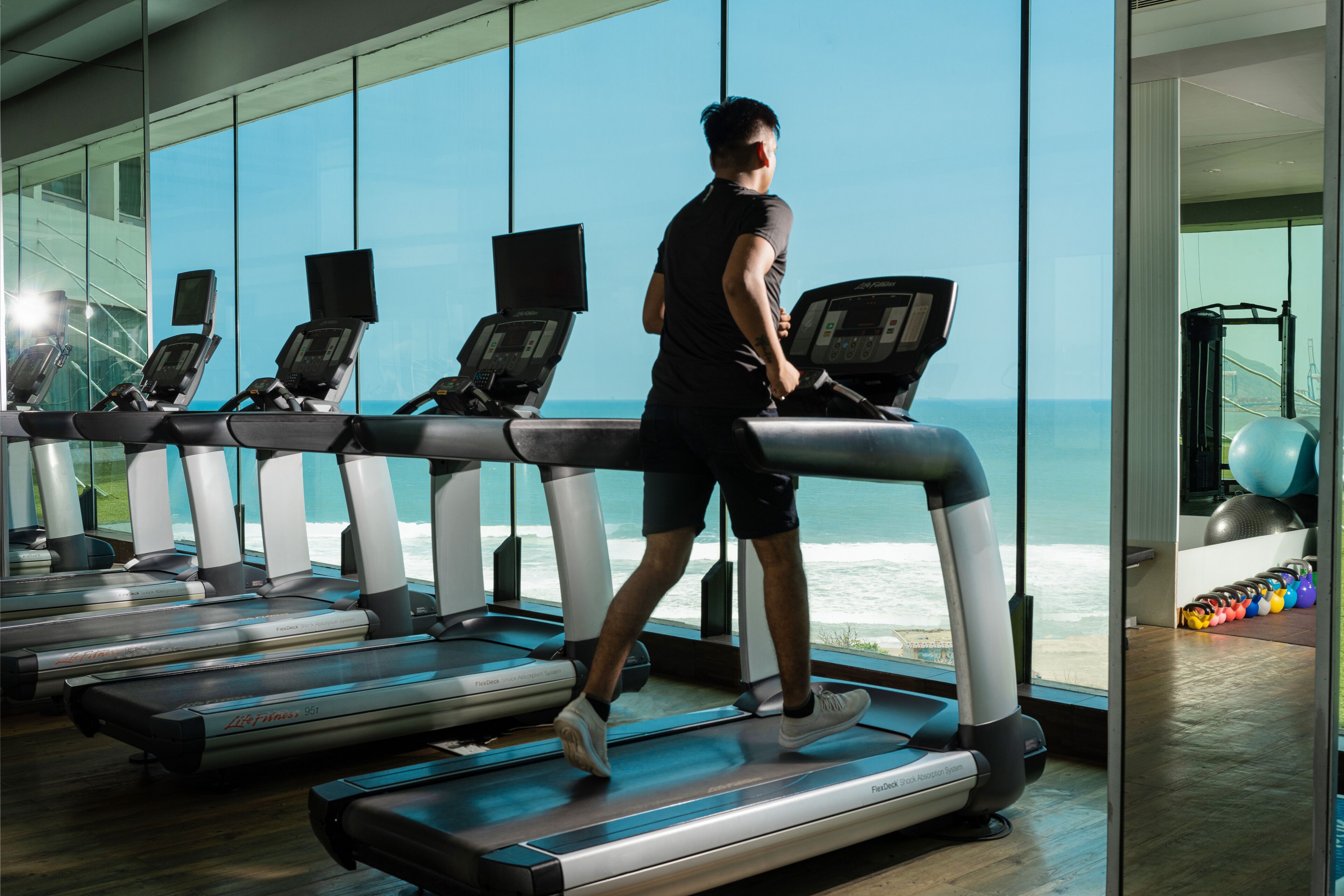 A gym with treadmills, exercise balls, and weights, overlooking a beach.