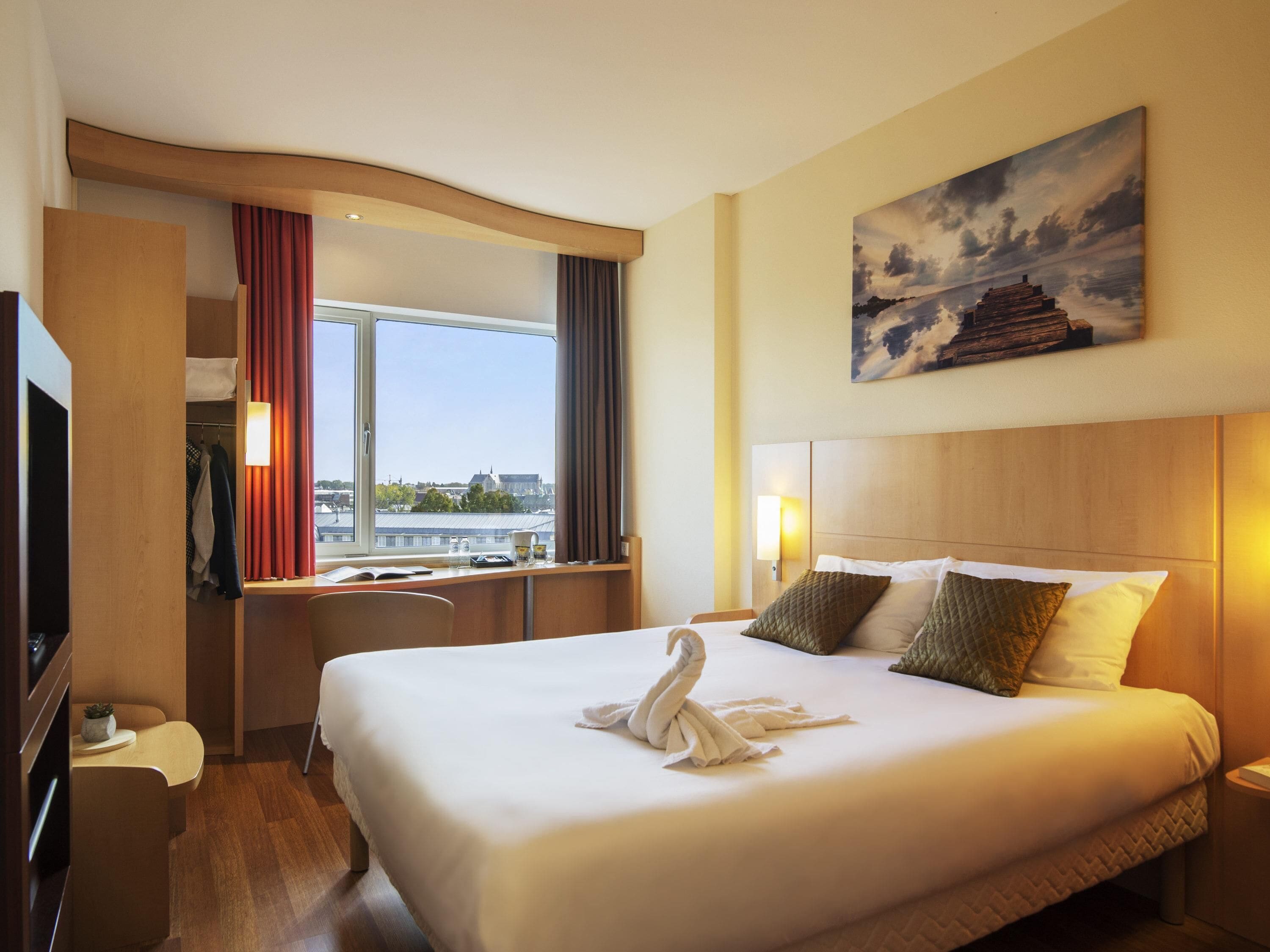 Una habitación de hotel con una cama grande, un escritorio, un televisor y una ventana con cortinas.