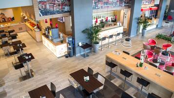 A modern hotel lobby with multiple dining areas, a bar, and a large cityscape view.