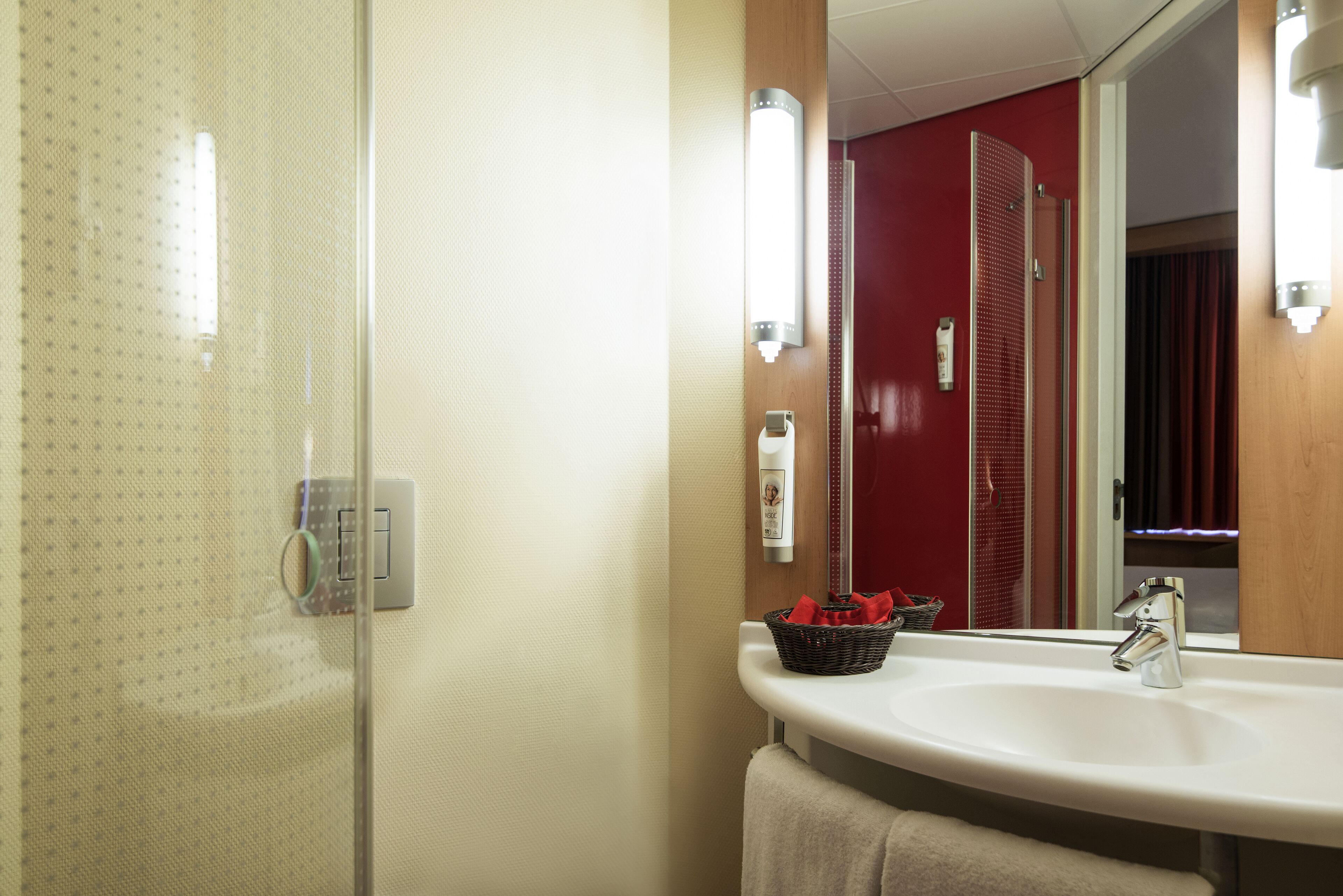 Un baño con un lavamanos blanco, un espejo y una puerta roja al fondo.