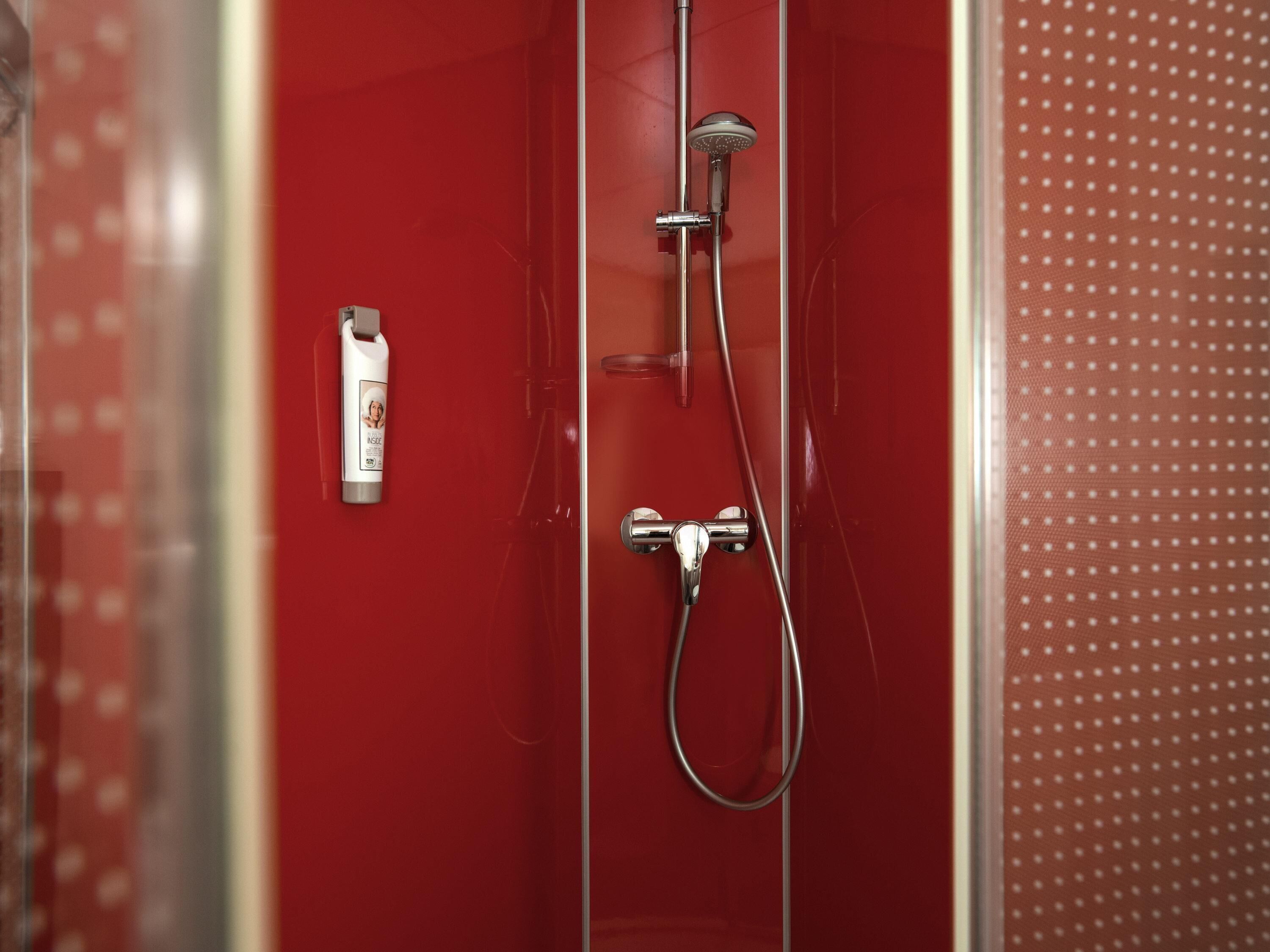 A red shower enclosure with a handheld showerhead and a handheld shower attachment.