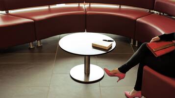 Une femme est assise sur un canapé rouge, un livre et un stylo sont posés sur une table ronde.