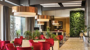 A modern hotel lobby with red chairs, large pendant lights, a reception desk, and a vertical garden wall. - ibis Leiden Centre (Leiden)