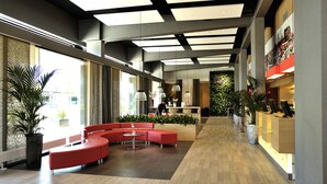 A spacious lobby with a curved red seating area, a reception desk, and a large window providing natural light. - ibis Leiden Centre (Leiden)