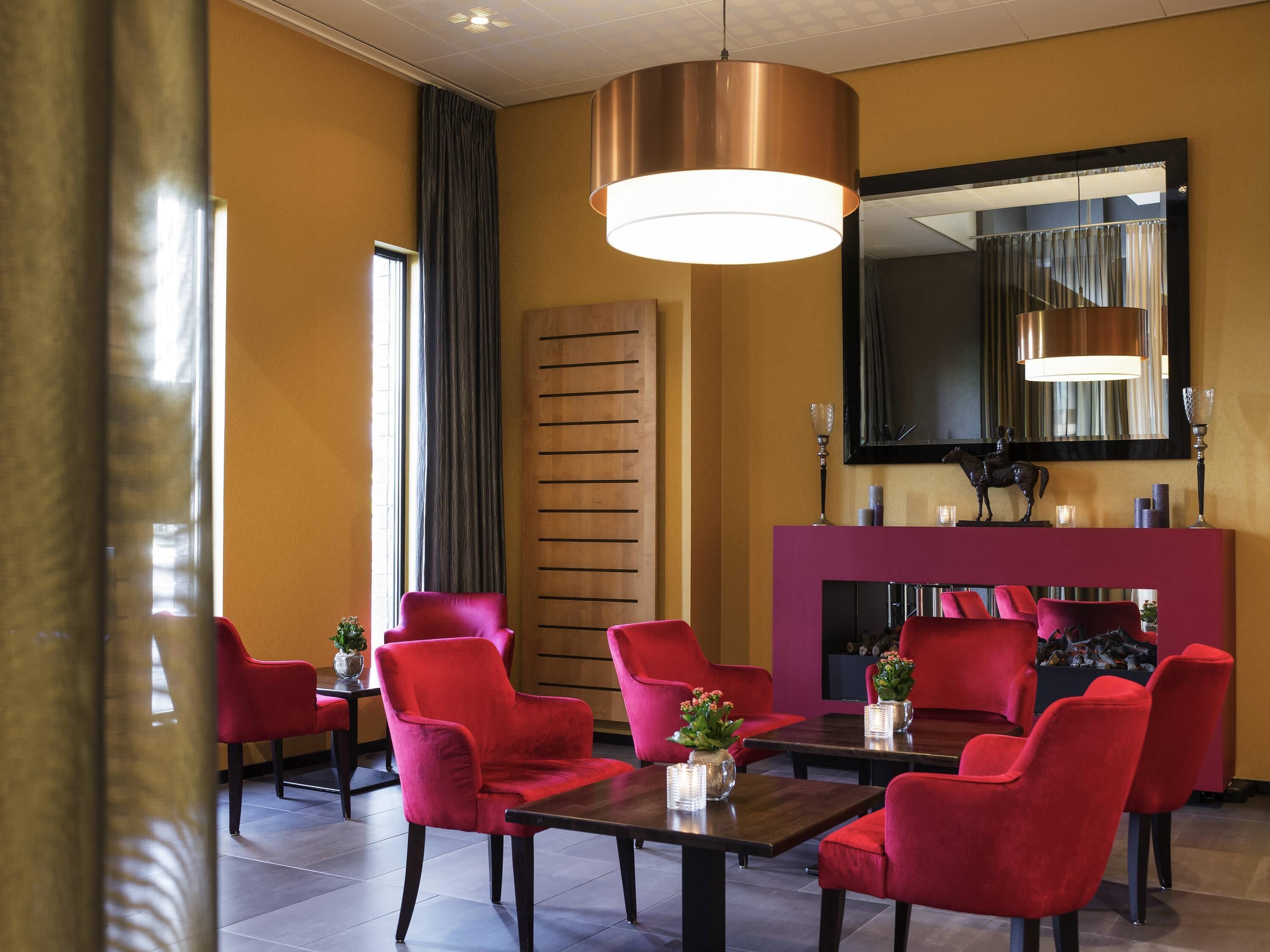 Un hall de hotel con sillas rojas, un panel de pared de madera, un espejo grande y una chimenea.