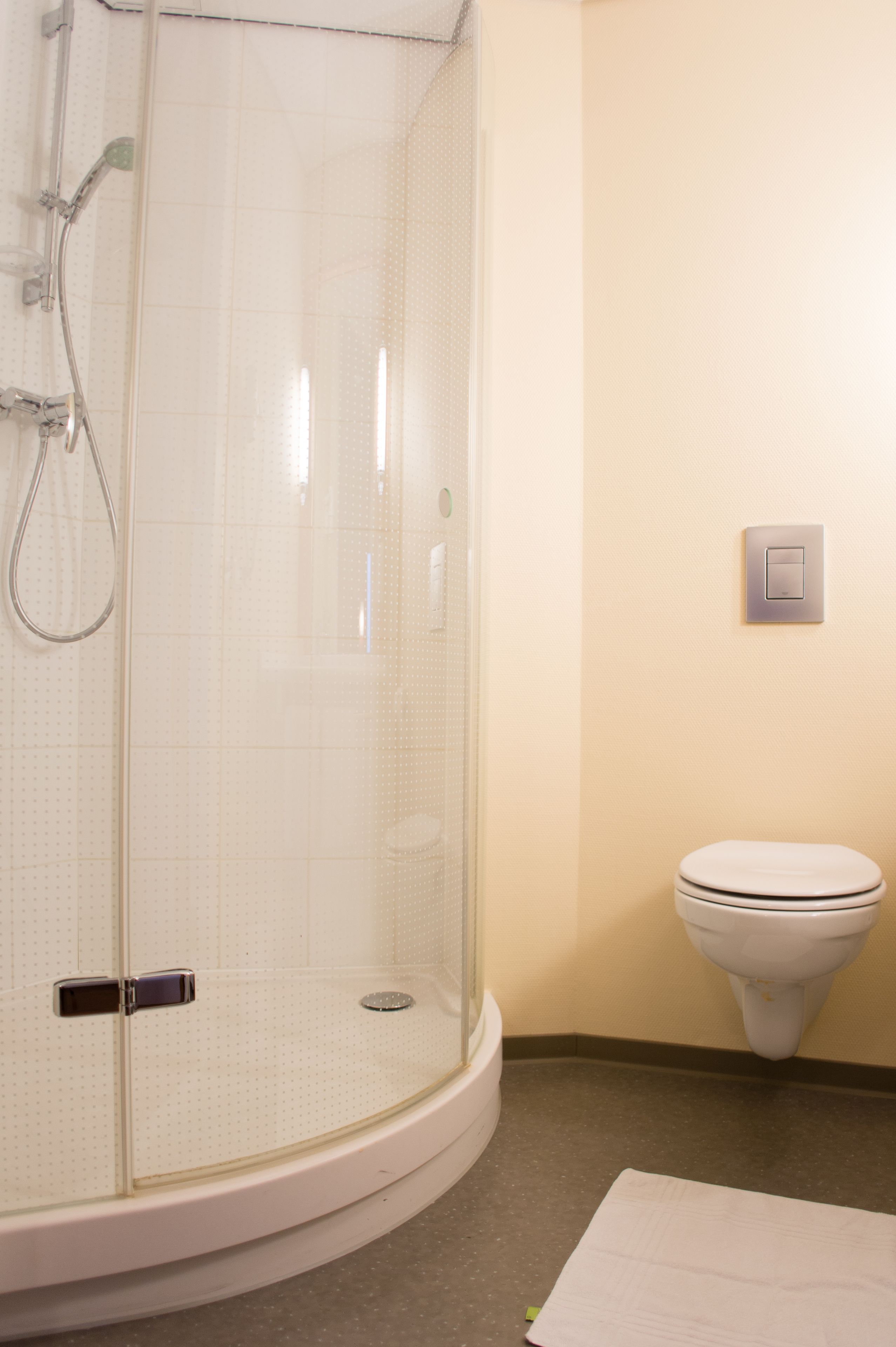 Un baño con ducha de vidrio, inodoro y un interruptor de luz en la pared.