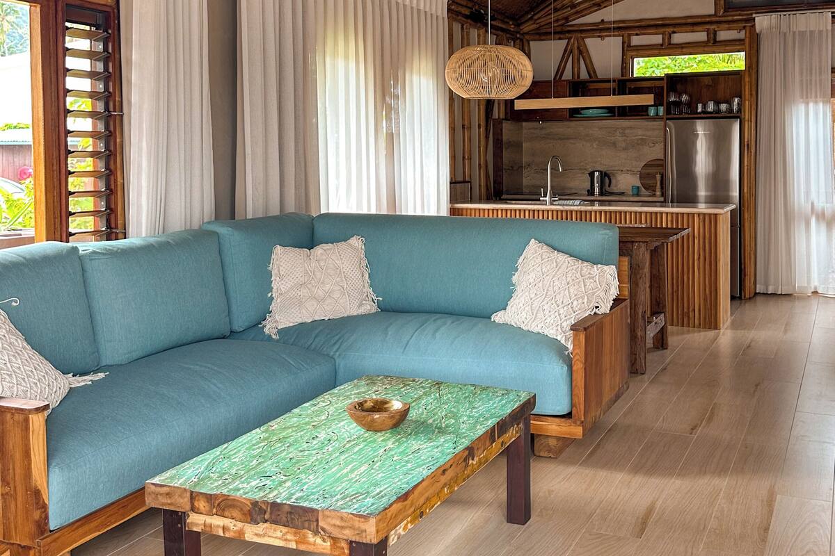 Ein gemütlicher Wohnbereich mit einem blauen Sofa, einem Holztisch und einer Küche im Hintergrund.