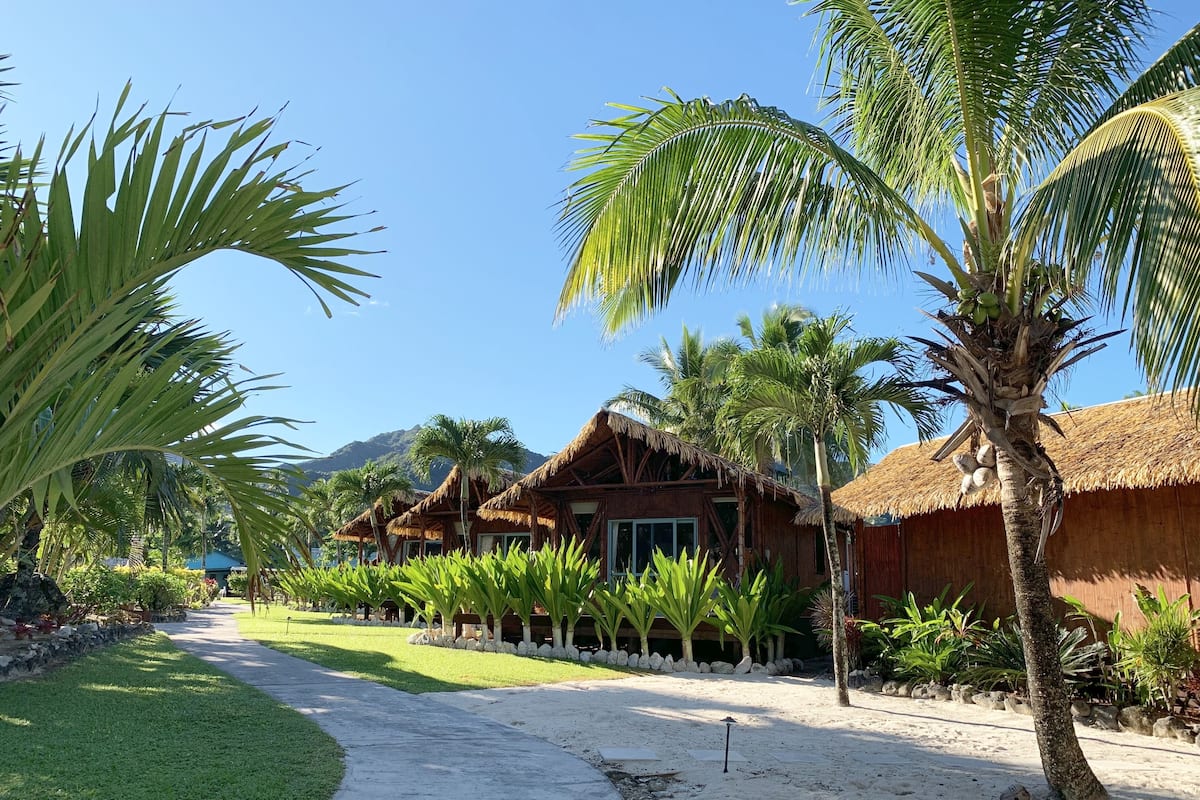 Ein Resort mit strohgedeckten Hütten, Palmen und blauem Himmel.