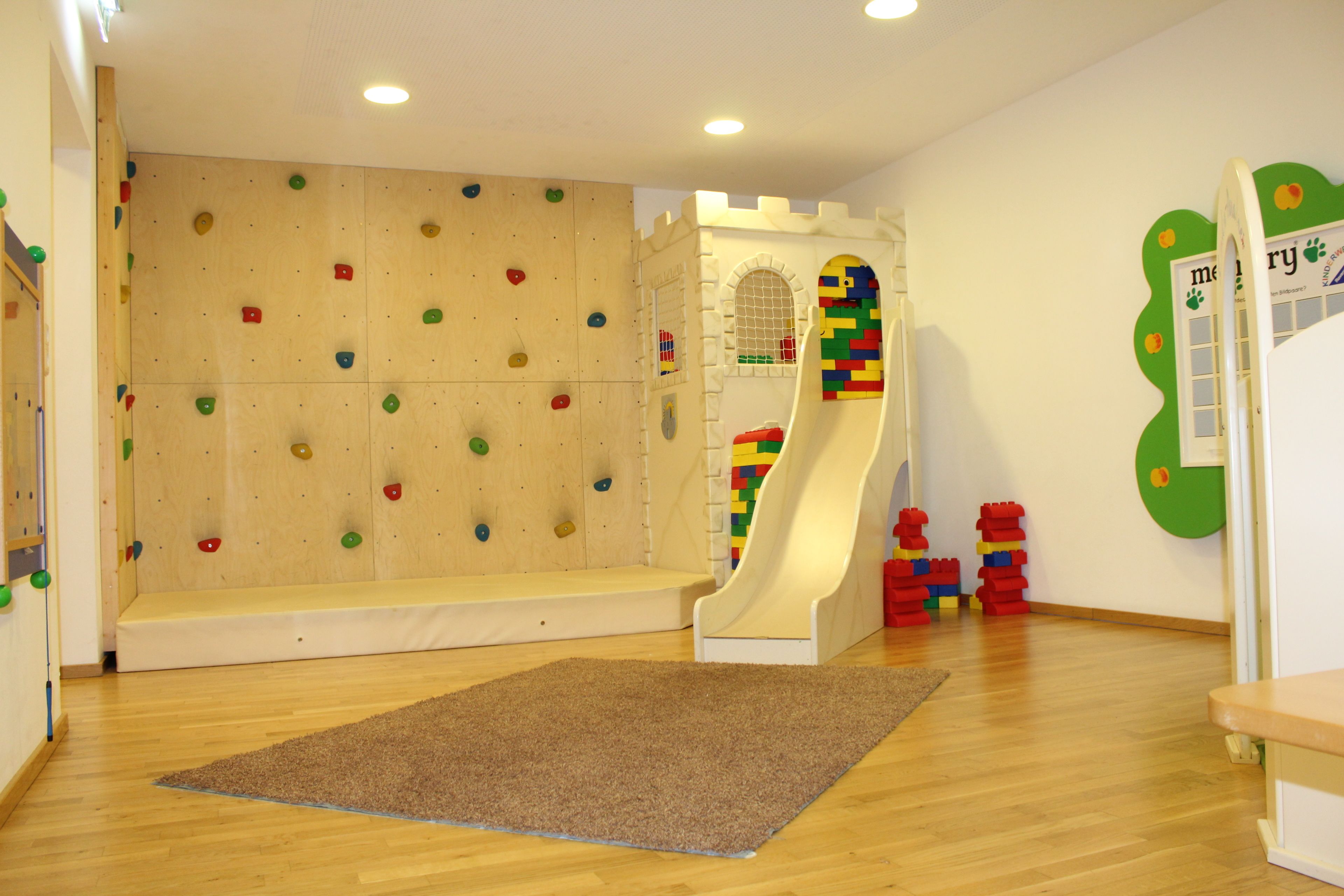 A playroom with a climbing wall, a slide, and colorful play structures.