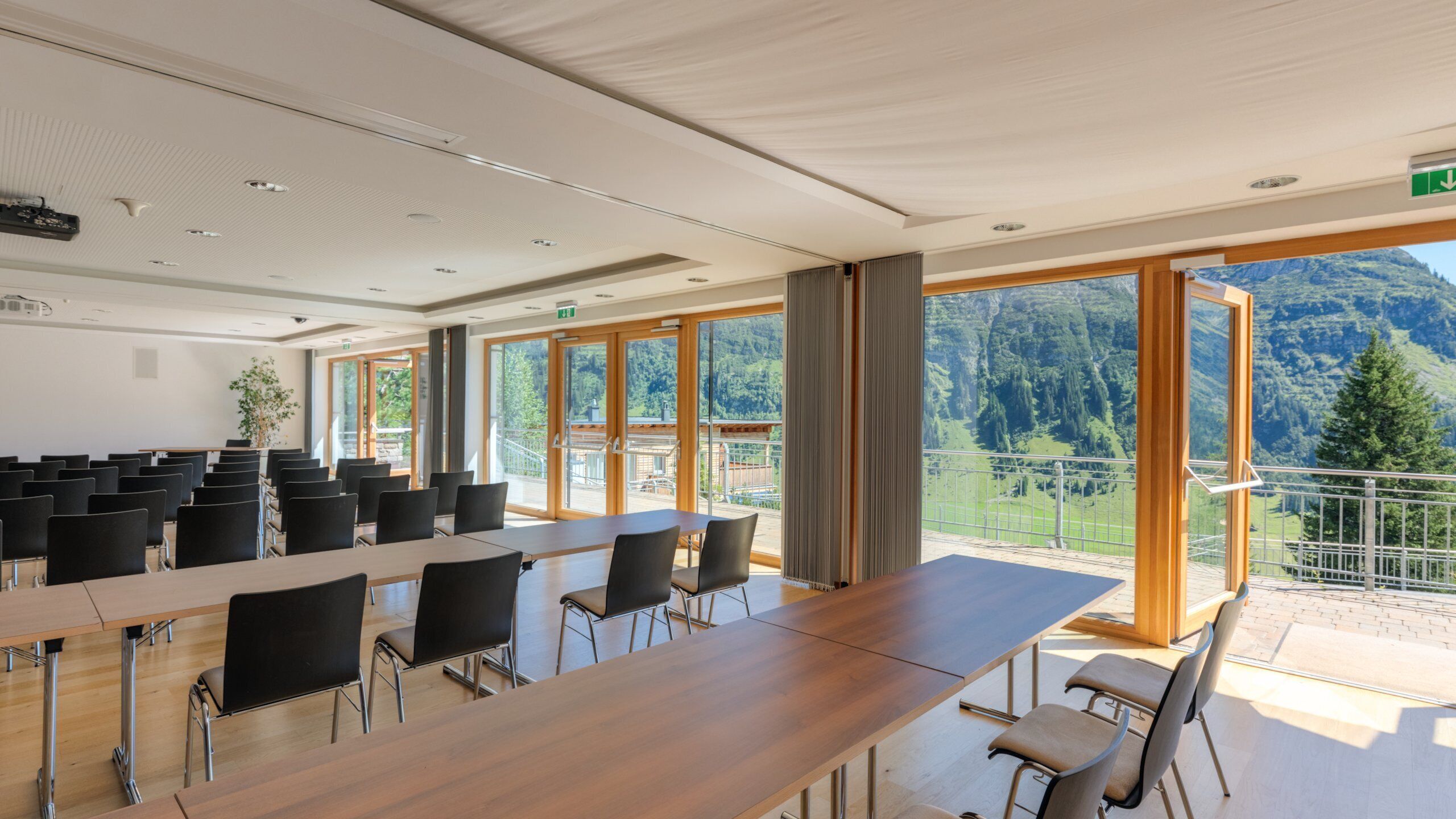 Un salón de conferencias con una larga mesa y sillas, amplias ventanas con vistas a la montaña e iluminación empotrada en el techo.