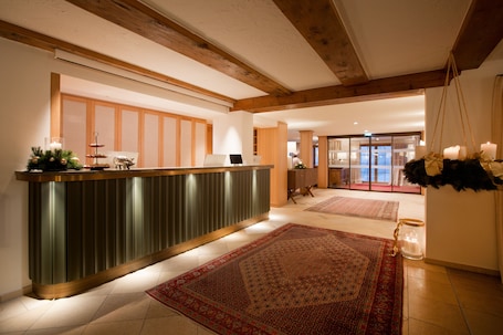 A reception area with a wooden reception desk, a large patterned rug, and a view of a balcony.