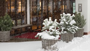 Un hotel con fachada amarilla y un letrero que dice 'HOTEL'. Hay plantas en macetas cubiertas de nieve en la parte delantera.