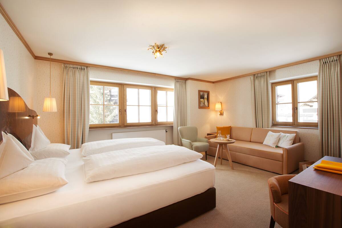 A hotel room with a large bed, a sofa, a chair, a small table, and a desk.