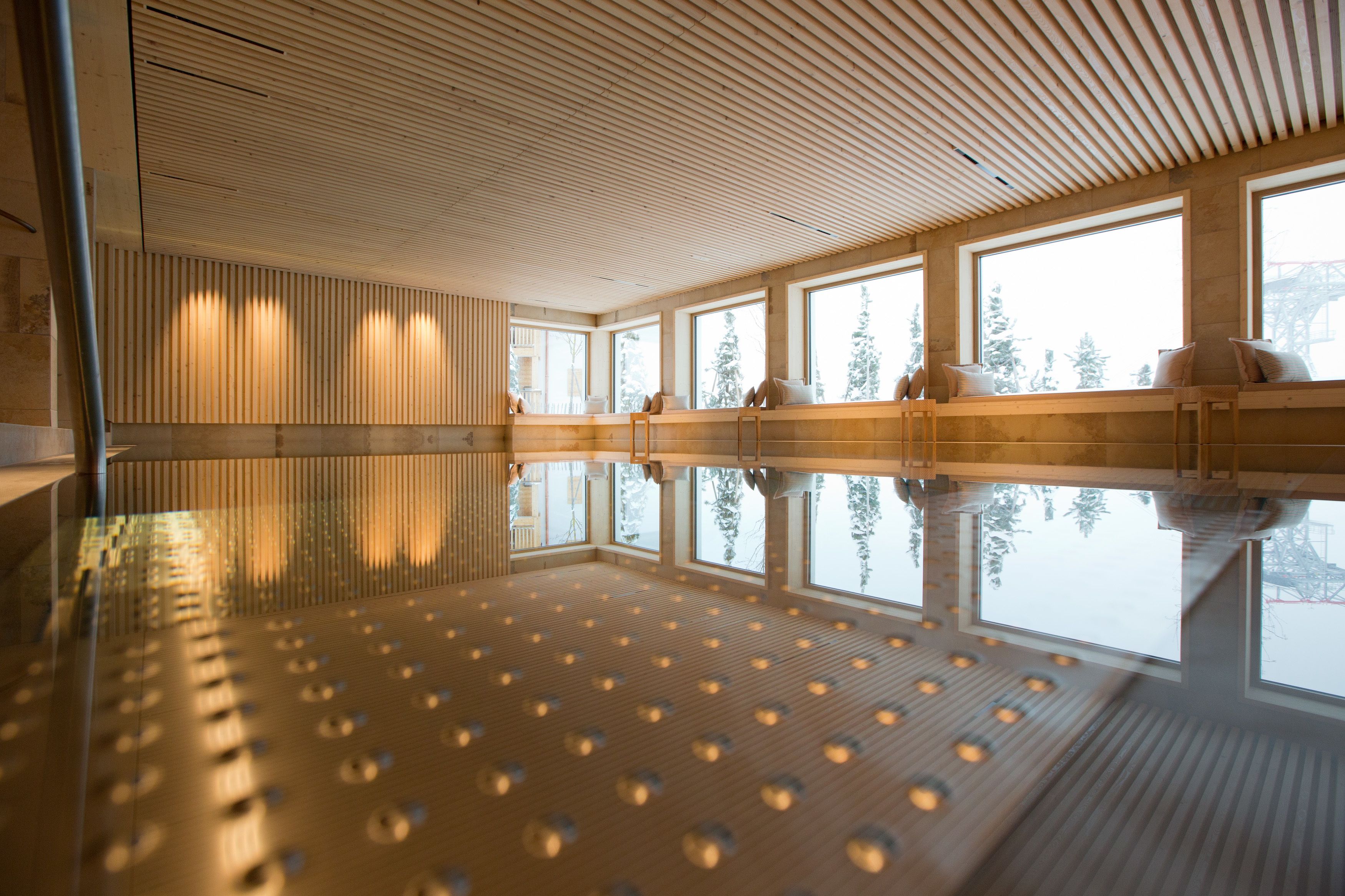 A modern indoor swimming pool with wooden slats on the ceiling and large windows.