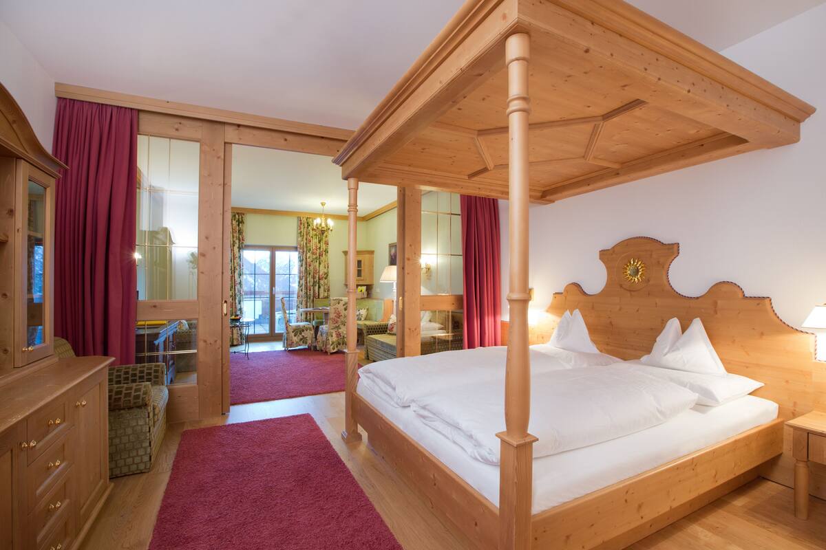 A wooden four-poster bed with white linens, a wooden dresser, and a red carpeted floor.